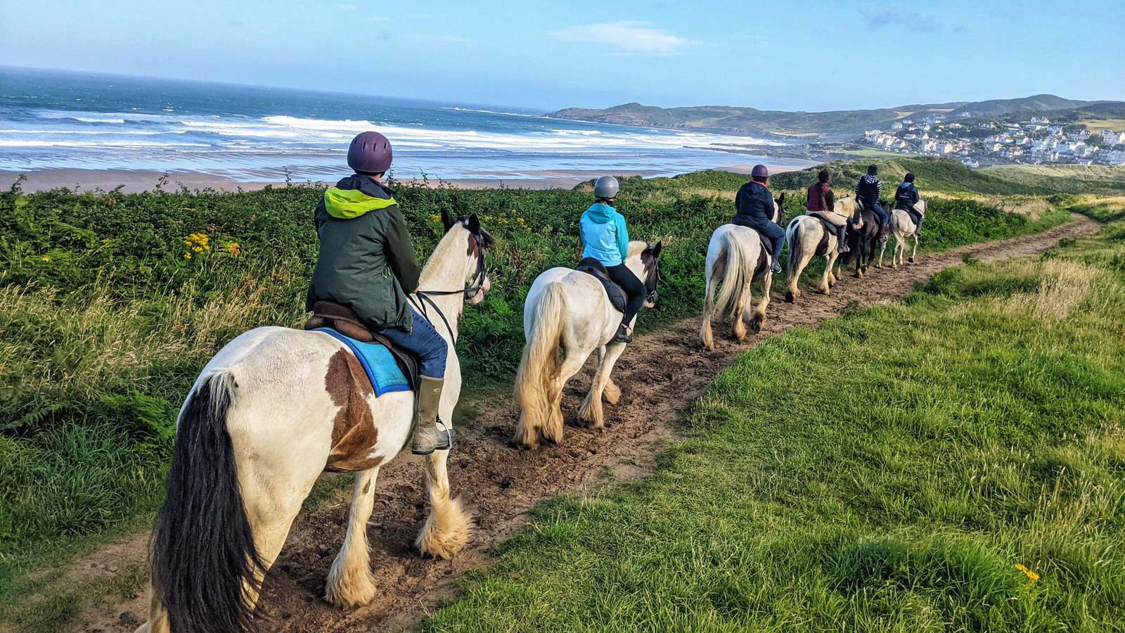 image of people on horses riding along the coast