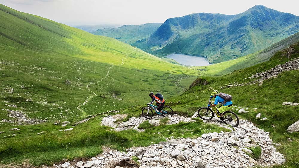 two mountain bikers riding down a hill in the lake district